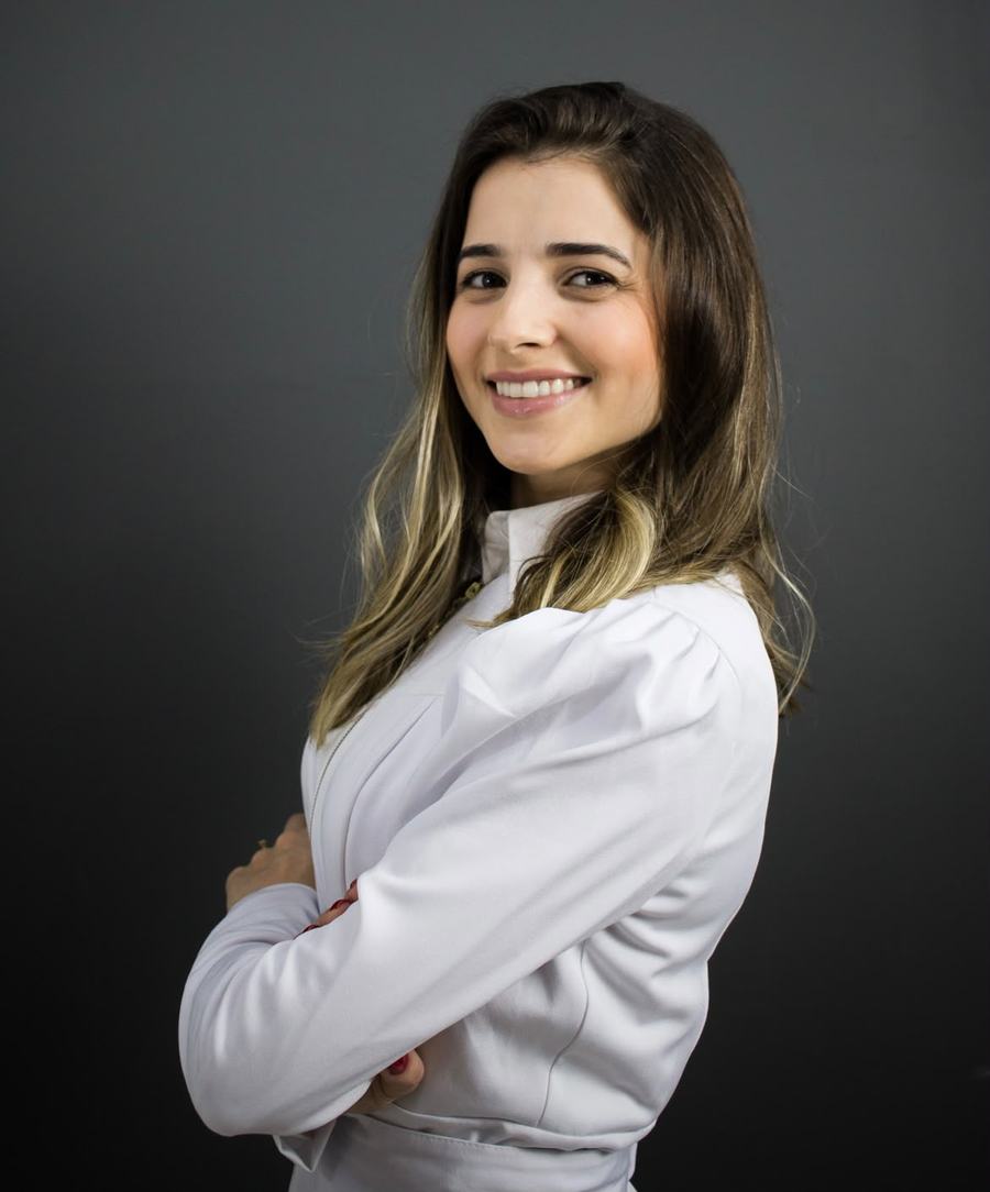 Dra. Jéssica Lessa, cirurgiã-dentista, de jaleco branco e braços cruzados, sorrindo